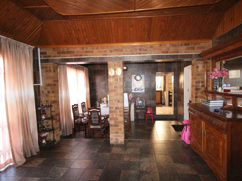 Open plan living and dining area featuring exposed brick columns, dark tiled flooring, and a distinctive timber tongue and groove ceiling.