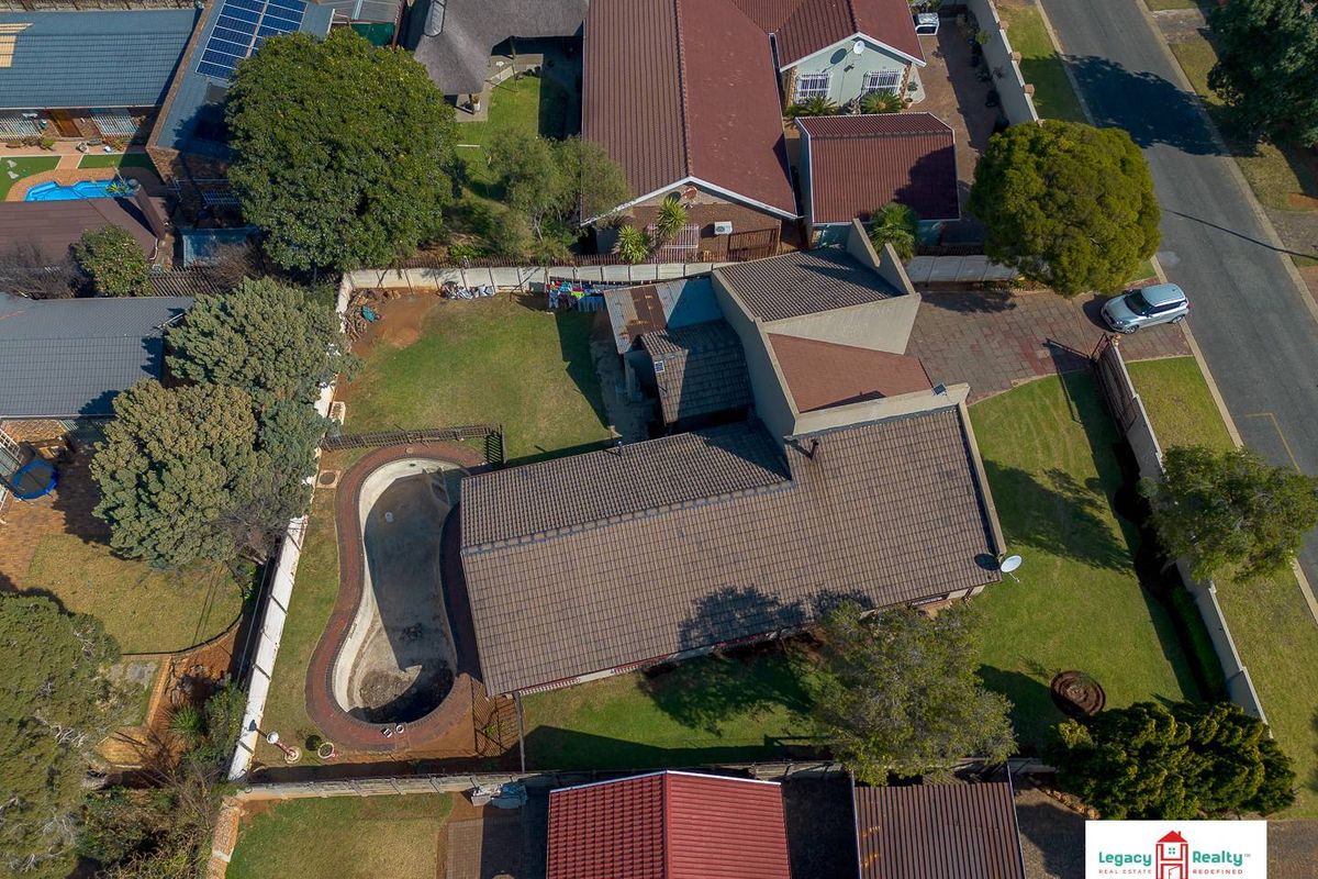 Aerial view of a residential property featuring a large garden, a swimming pool, and a tiled roof structure.