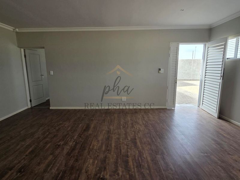 Spacious, empty living area featuring dark laminate flooring, coved ceilings, and white plantation shutters with direct access to an outdoor area.