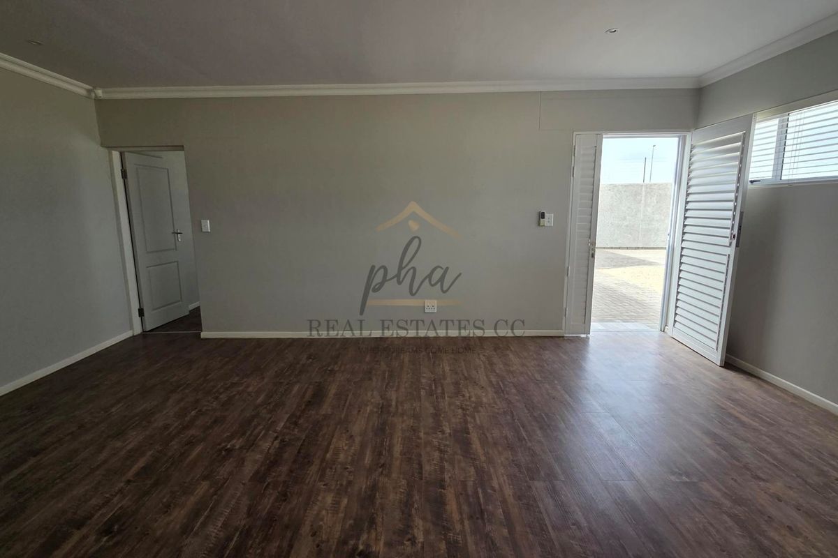 Spacious, empty living area featuring dark laminate flooring, coved ceilings, and white plantation shutters with direct access to an outdoor area.