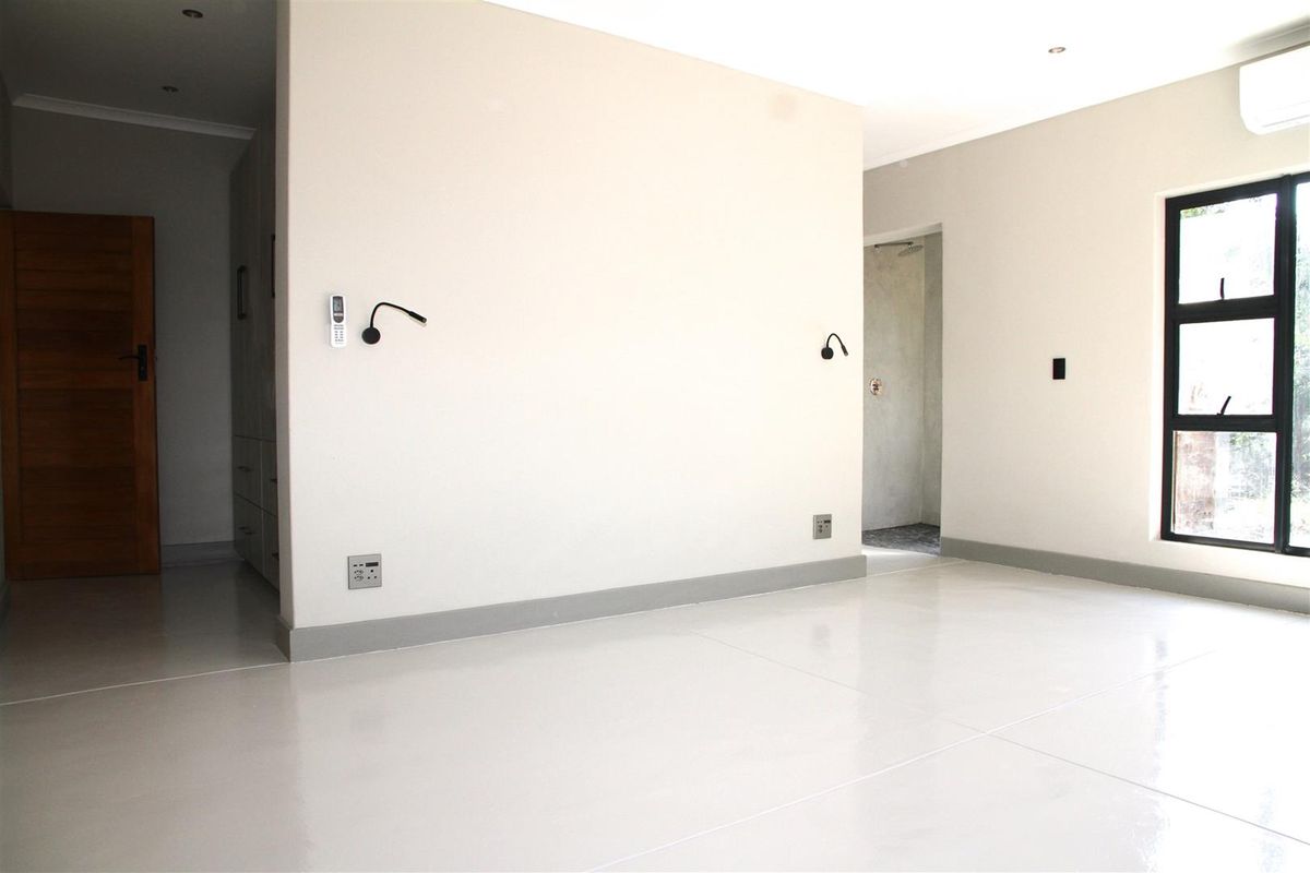 A bright, modern bedroom featuring polished concrete flooring, built-in wall lighting, and an en-suite bathroom access point.