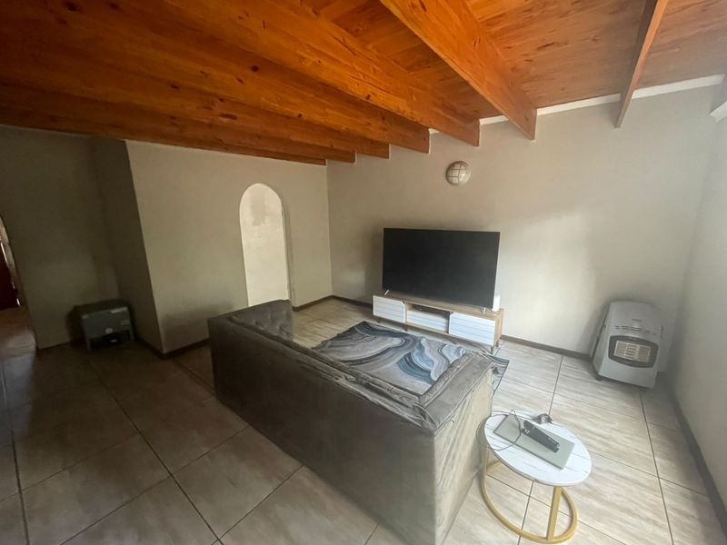 Living room featuring exposed timber ceiling beams, tiled flooring, and an arched doorway leading to an adjacent space.