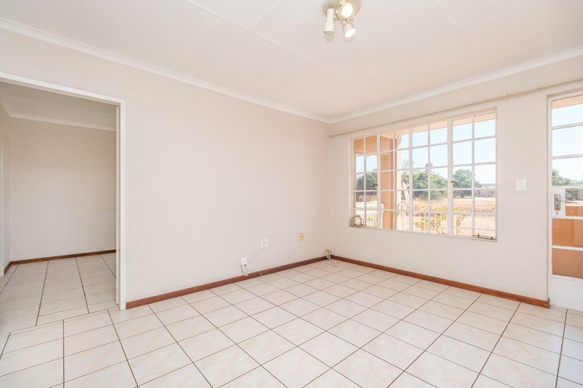 A bright, empty living area featuring neutral tiled flooring, large grid-pattern windows, and direct access to an outdoor space.