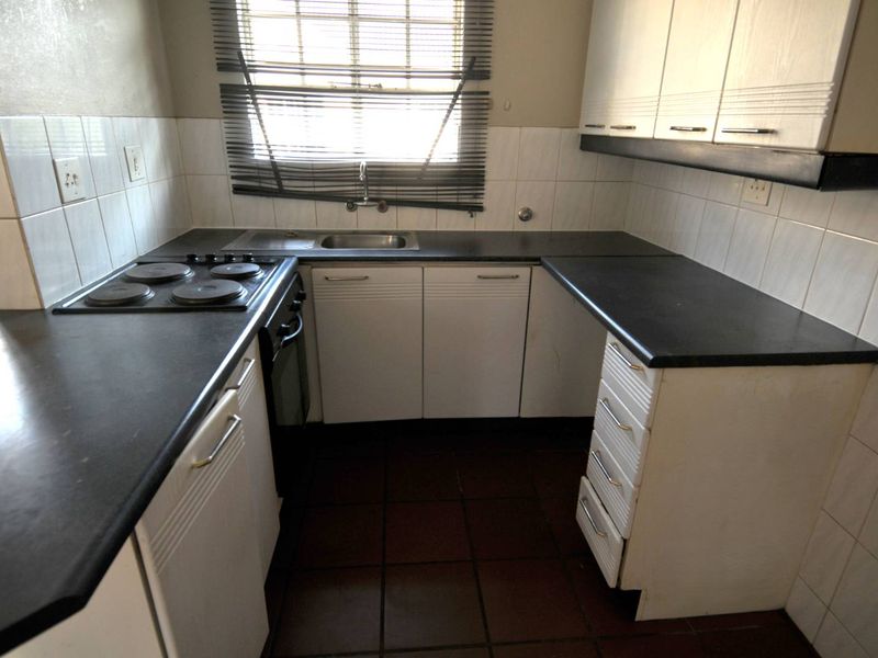 A compact, functional kitchen featuring white cabinetry, dark laminate countertops, an electric hob, and tiled finishes, ready for a modern update.