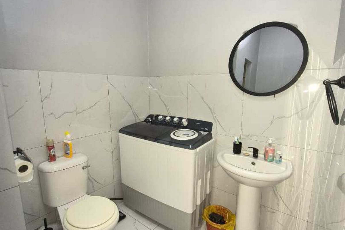 A functional bathroom featuring marble-look wall and floor tiles, a pedestal sink, and a toilet, with space for laundry appliances.