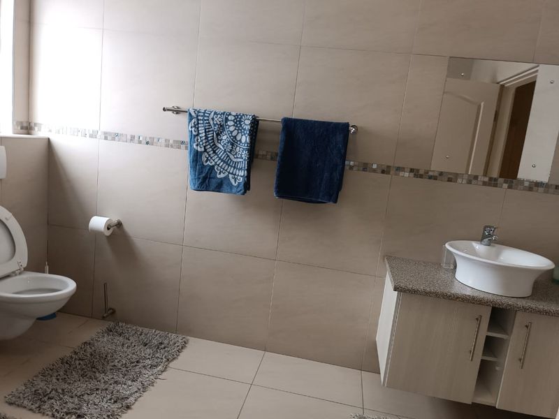 A functional bathroom featuring a wall-mounted toilet, a modern vanity cabinet with a countertop basin, and neutral wall tiling with a decorative mosaic border.