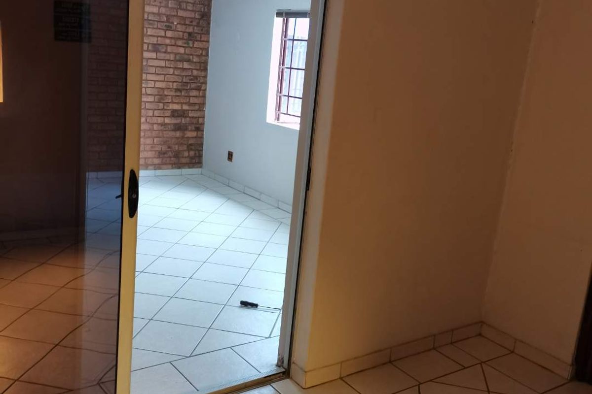 An empty living area featuring ceramic floor tiles, an exposed brick feature wall, and a sliding glass door leading to an adjacent space.