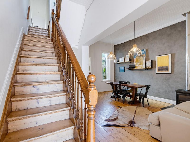 Open plan living area featuring a classic timber staircase, hardwood flooring, and a wood-burning stove with a feature wall.
