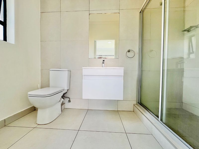A clean, modern bathroom featuring a wall-mounted vanity, a glass-enclosed shower, and neutral floor-to-ceiling tiling.