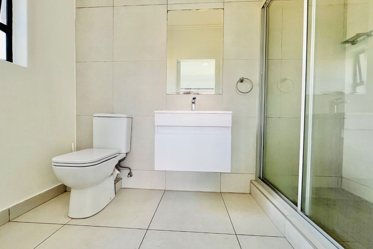 A clean, modern bathroom featuring a wall-mounted vanity, a glass-enclosed shower, and neutral floor-to-ceiling tiling.