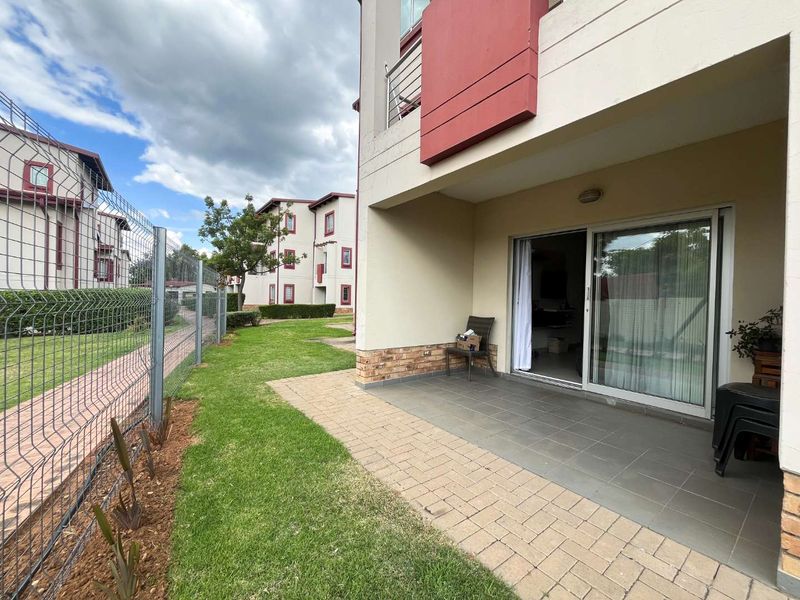 A ground floor patio area featuring tiled flooring and a sliding glass door, overlooking a communal garden space with perimeter fencing.