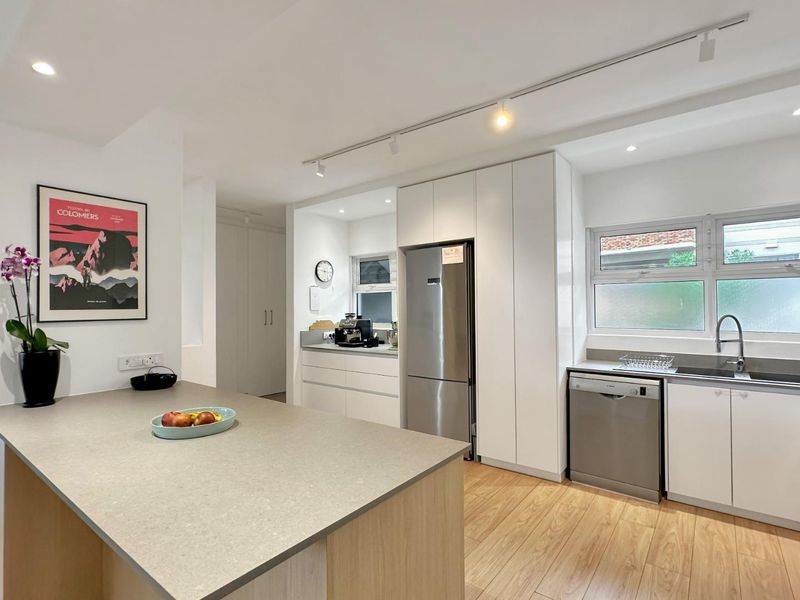 Modern, well-maintained kitchen featuring a central island with stone countertops, sleek white cabinetry, integrated appliances, and bright track lighting.