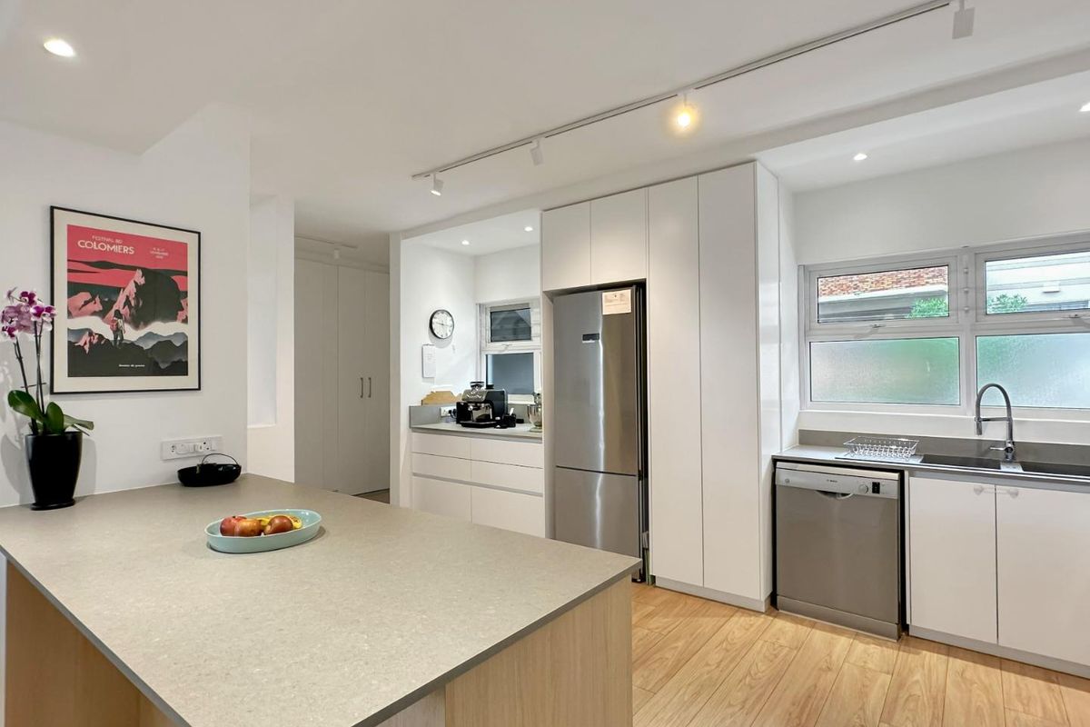 Modern, well-maintained kitchen featuring a central island with stone countertops, sleek white cabinetry, integrated appliances, and bright track lighting.
