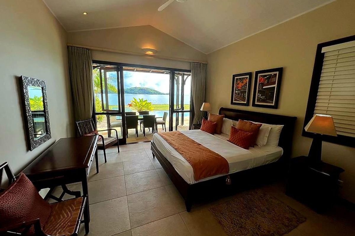 Spacious bedroom featuring vaulted ceilings, tiled flooring, and large glass doors opening onto a private patio with scenic water views.