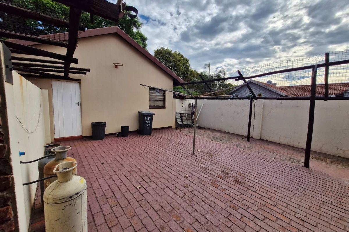 A paved rear courtyard area featuring boundary walls, a metal pergola structure, and direct access to the main dwelling.