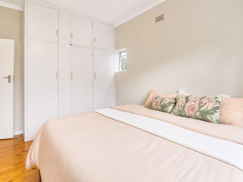 A bright bedroom featuring polished timber flooring and ample built-in cupboard storage with a neutral color palette.
