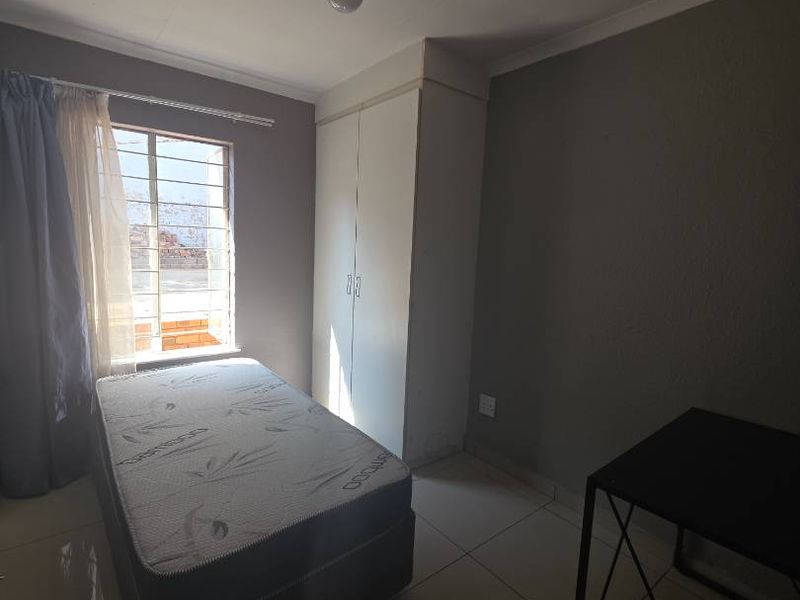 A bedroom featuring tiled flooring, a built-in wardrobe, and a window fitted with security burglar bars.