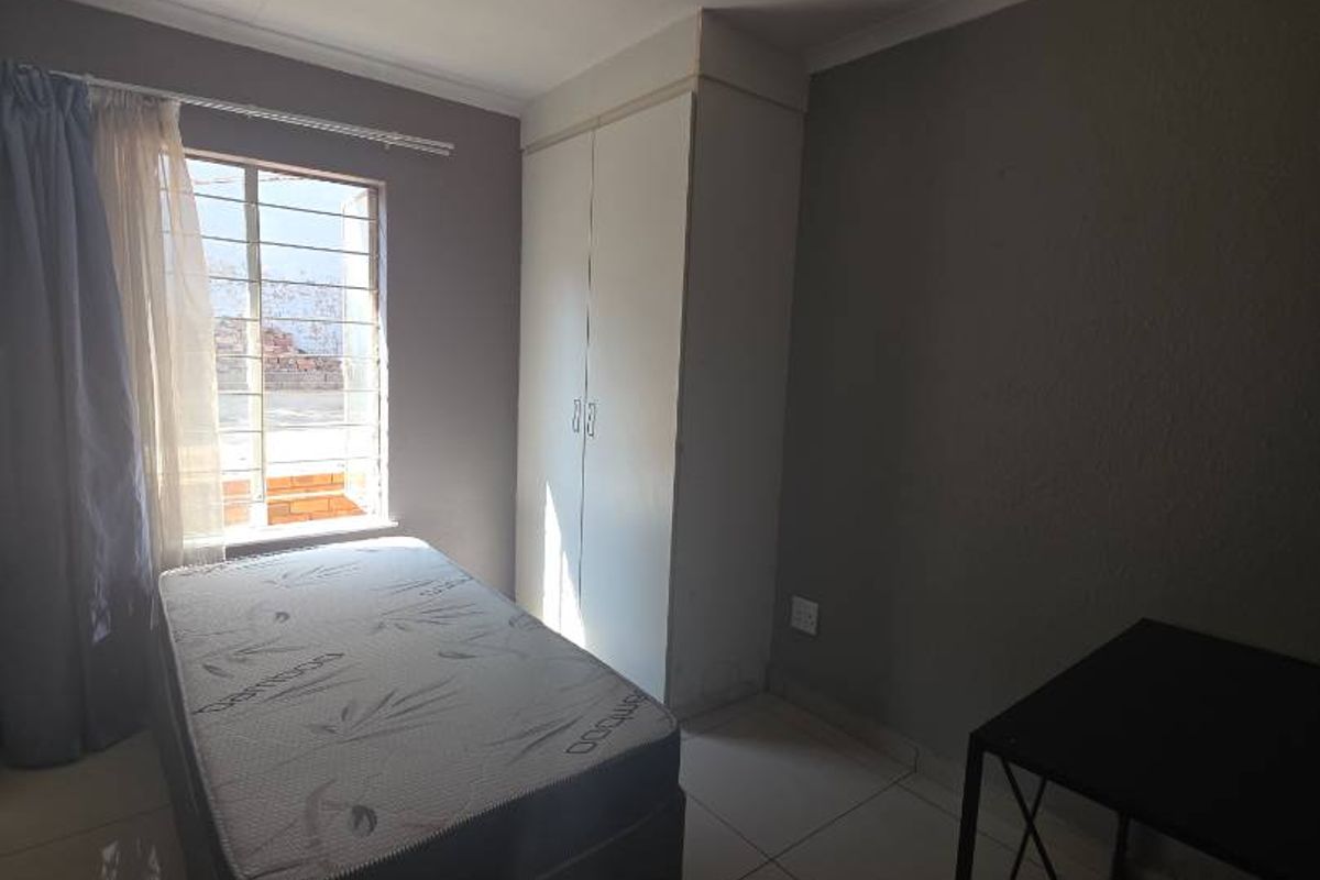 A bedroom featuring tiled flooring, a built-in wardrobe, and a window fitted with security burglar bars.