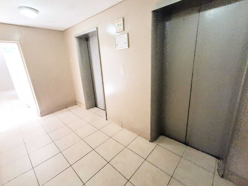 A functional apartment building hallway featuring tiled flooring and elevator access.