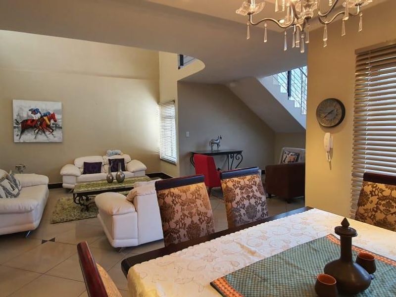 Spacious open-plan living and dining area featuring tiled floors, a staircase, and large windows with venetian blinds.
