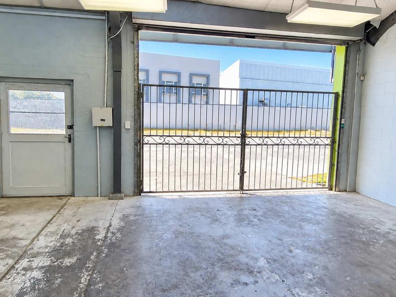 Spacious industrial garage area featuring concrete flooring, secure metal gate access, and functional overhead lighting, suitable for storage or workshop use.