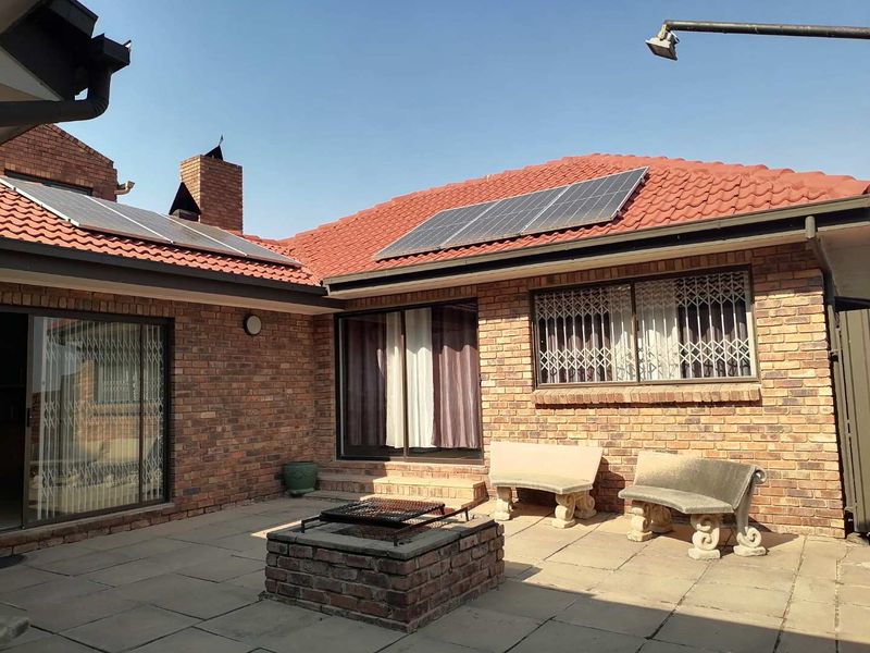 A paved outdoor patio area featuring a built-in brick fireplace, sliding door access to the home, and roof-mounted solar panels.