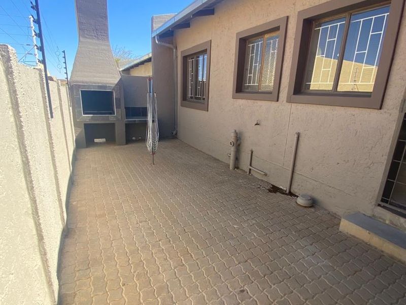 Rear exterior area featuring a paved patio, built-in braai, and secure boundary wall with electric fencing.