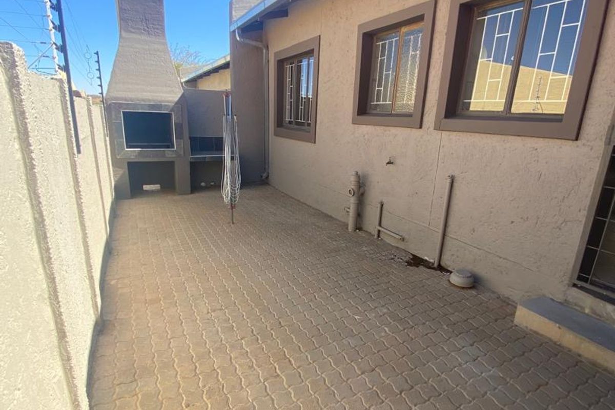 Rear exterior area featuring a paved patio, built-in braai, and secure boundary wall with electric fencing.