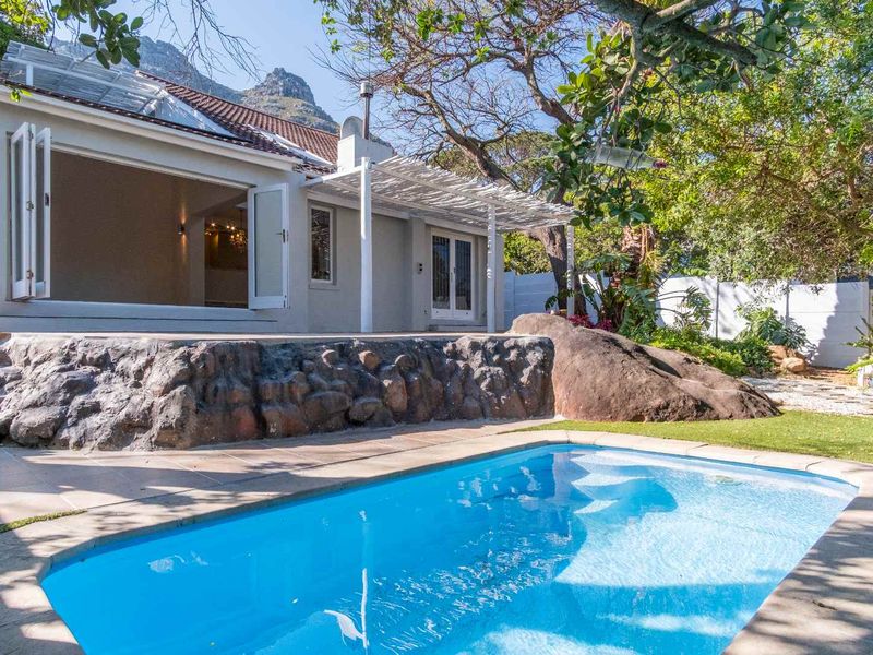 A well-maintained outdoor pool area featuring a stone retaining wall, a shaded pergola, and seamless indoor-outdoor flow through large bi-fold doors.
