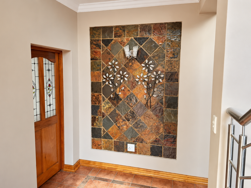 A well-maintained hallway featuring a decorative slate tile accent wall, stained glass timber door, and modern stainless steel balustrade.