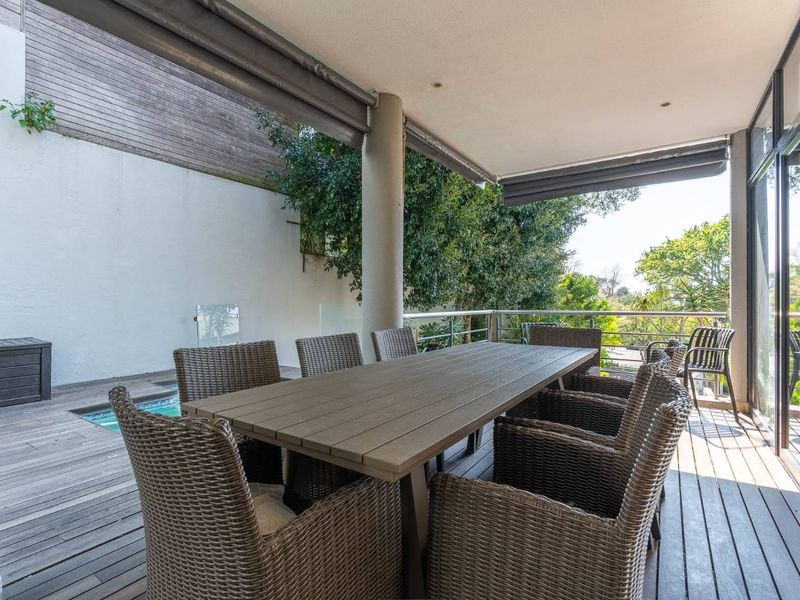 Spacious covered patio featuring timber decking, stainless steel balustrades, and retractable blinds, offering a functional outdoor entertainment area.