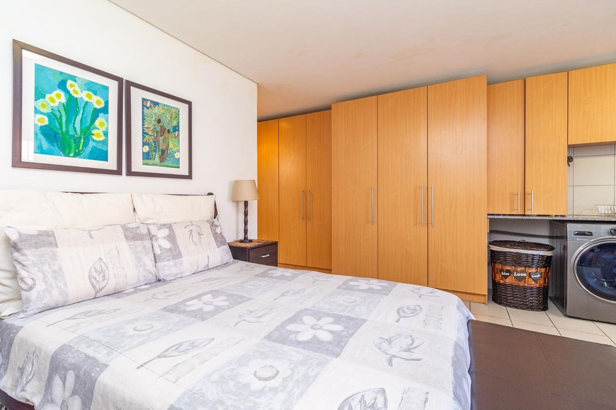 A bedroom featuring built-in wooden cupboards and tiled flooring, with an integrated laundry nook containing a washing machine connection.