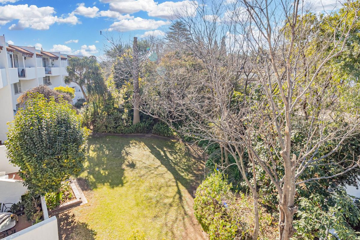 An elevated view of the apartment complex rear garden, featuring established trees, lawn space, and private balconies overlooking the outdoor area.