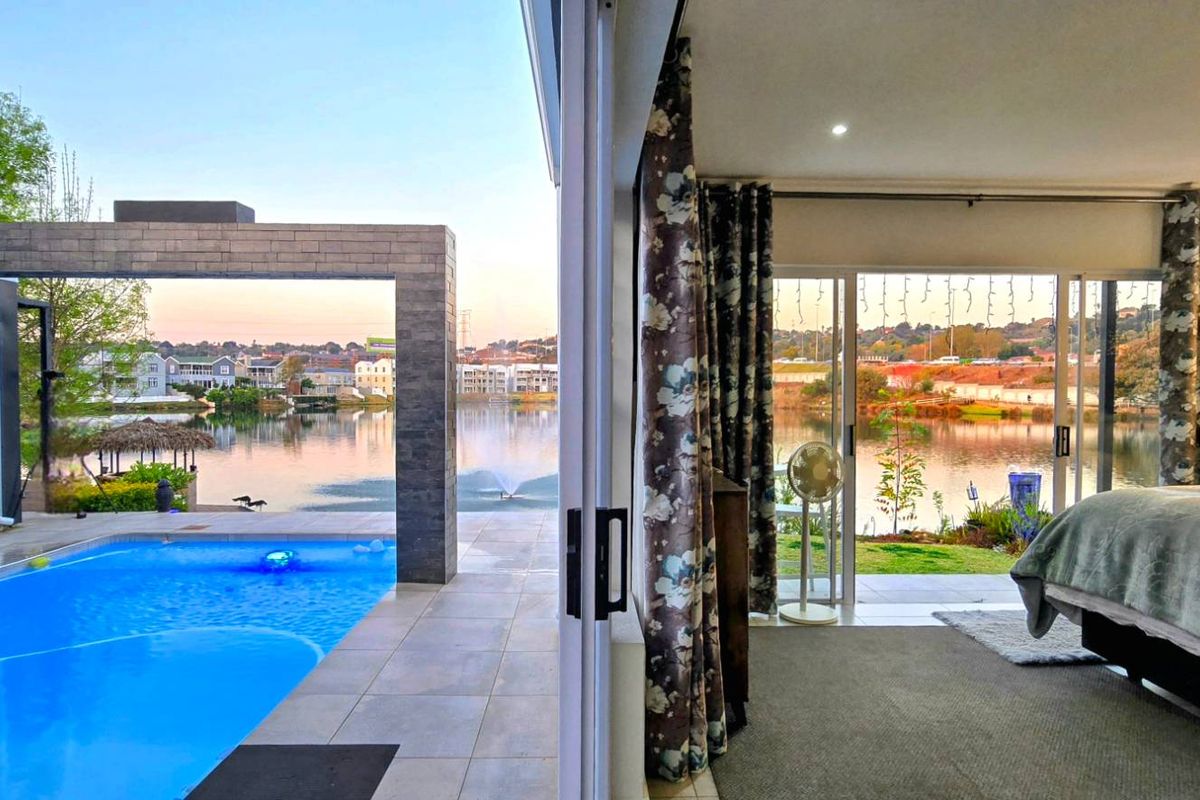 A luxurious bedroom featuring large sliding glass doors that open onto a private patio with a swimming pool and scenic lake views.