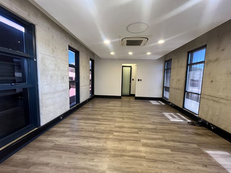 Modern, empty office space featuring exposed concrete walls, laminate wood flooring, recessed lighting, and ducted air conditioning, offering a clean and professional work environment.