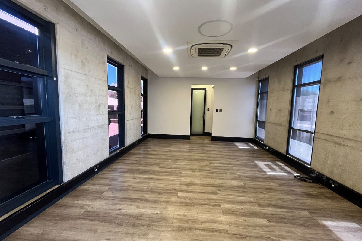 Modern, empty office space featuring exposed concrete walls, laminate wood flooring, recessed lighting, and ducted air conditioning, offering a clean and professional work environment.