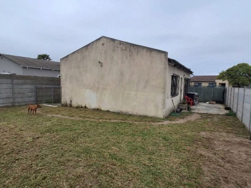 Rear view of the property featuring a large backyard enclosed by precast concrete boundary walls and a metal security gate.