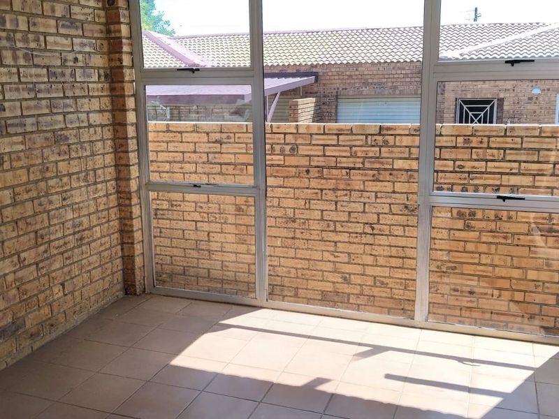 A covered patio area featuring face brick walls, tiled flooring, and large aluminium-framed windows overlooking the rear exterior space.