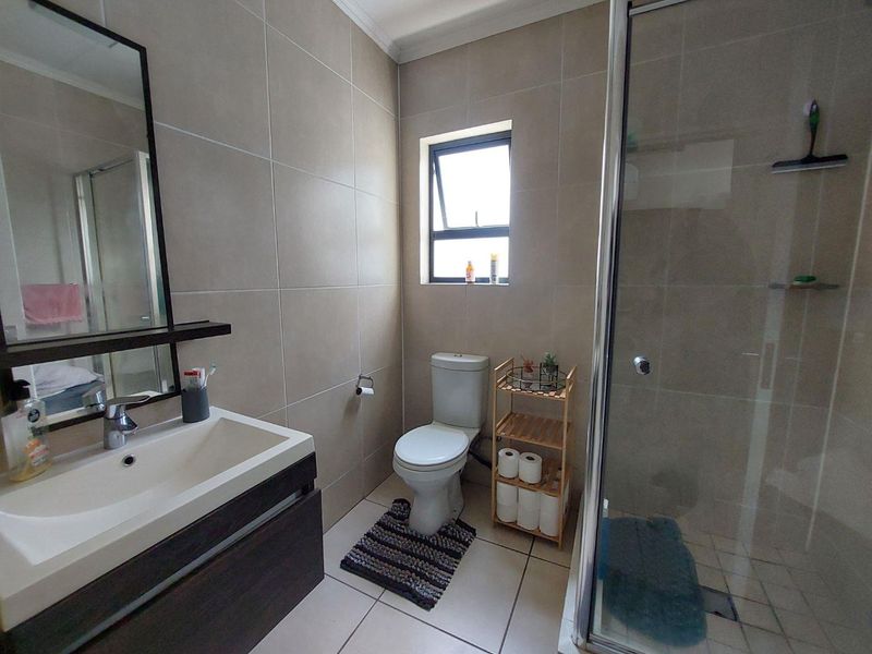 A modern bathroom featuring neutral wall tiles, a vanity with basin, a toilet, and a glass-enclosed shower.