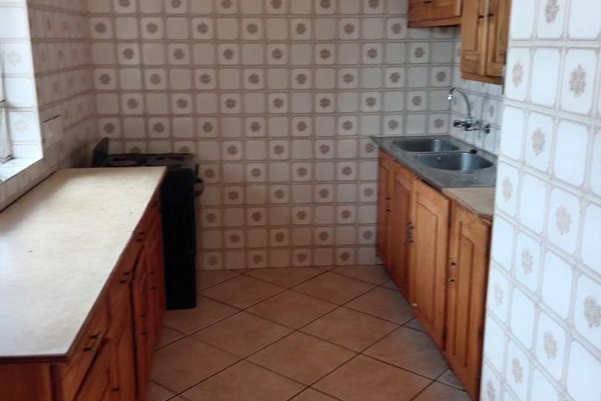 A dated kitchen featuring wooden cabinetry, laminate countertops, a double bowl stainless steel sink, and full-height ceramic wall tiling.