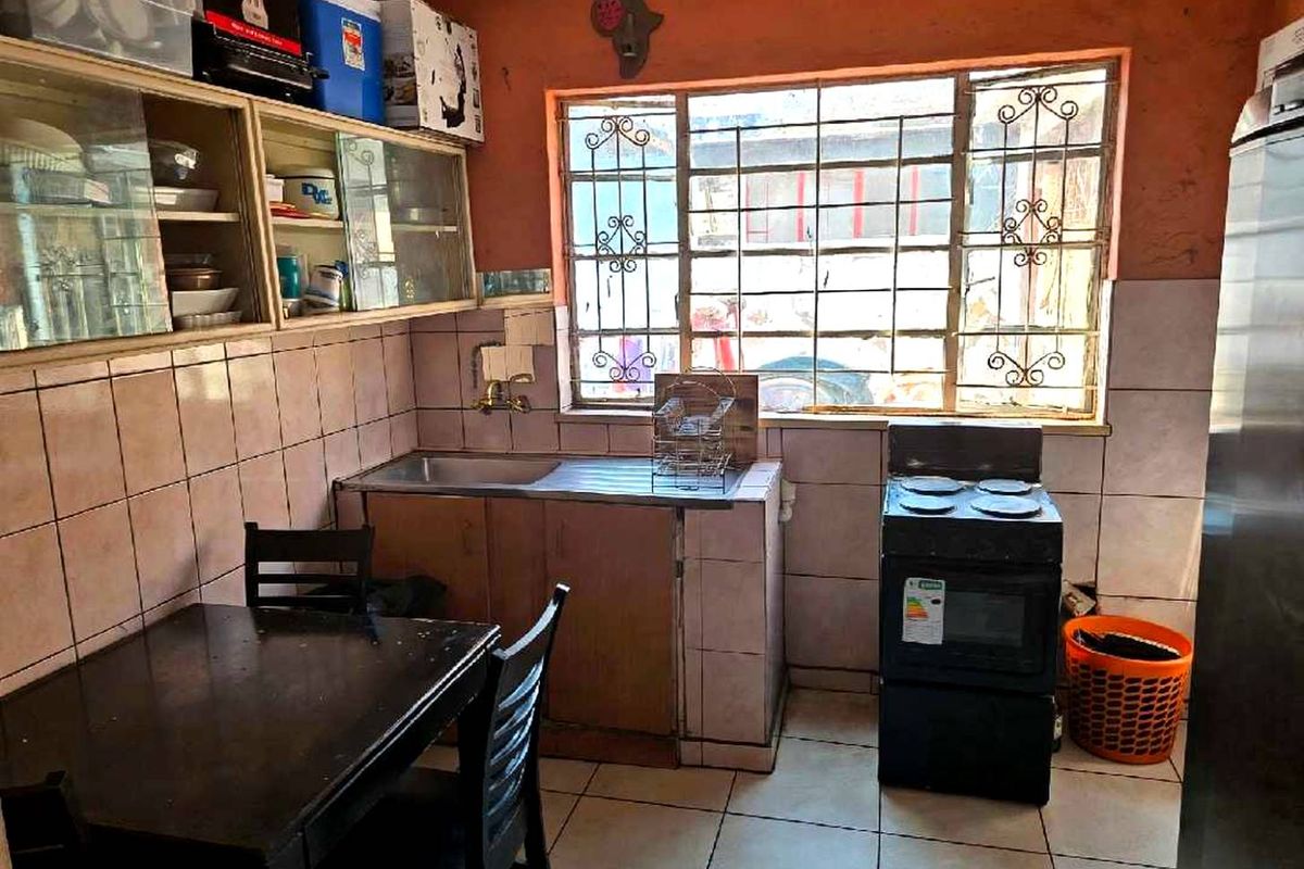 A functional kitchen featuring tiled walls and flooring, built-in cabinetry, a stainless steel sink, and a window with security bars.
