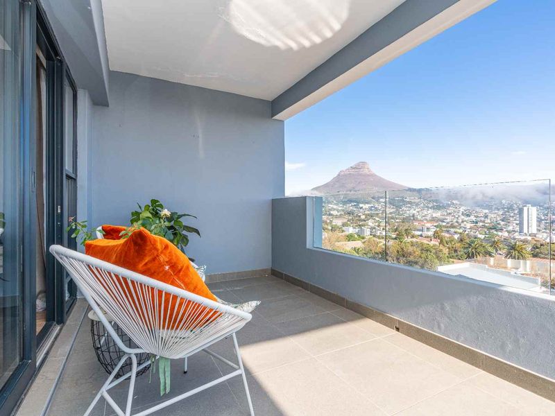 A modern balcony featuring tiled flooring and a sleek glass balustrade, offering expansive views of the city and mountain.