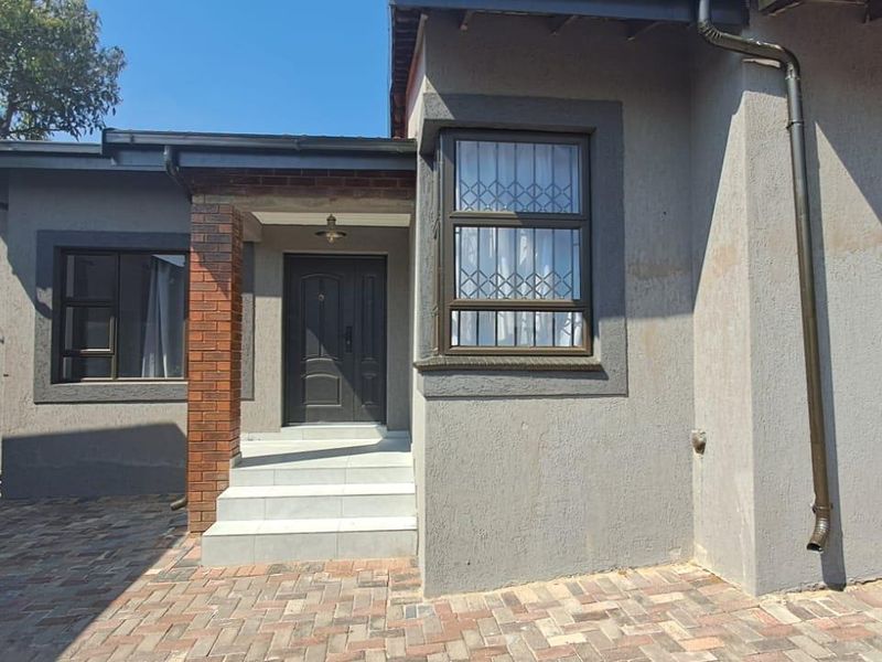 Front entrance of the house featuring a paved driveway, tiled steps, and security-fitted windows with a modern grey exterior finish.