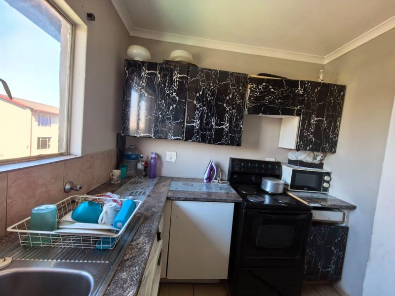 A compact kitchen featuring dark marble-effect cabinetry, laminate countertops, a stainless steel sink, and a freestanding stove with a tiled backsplash.
