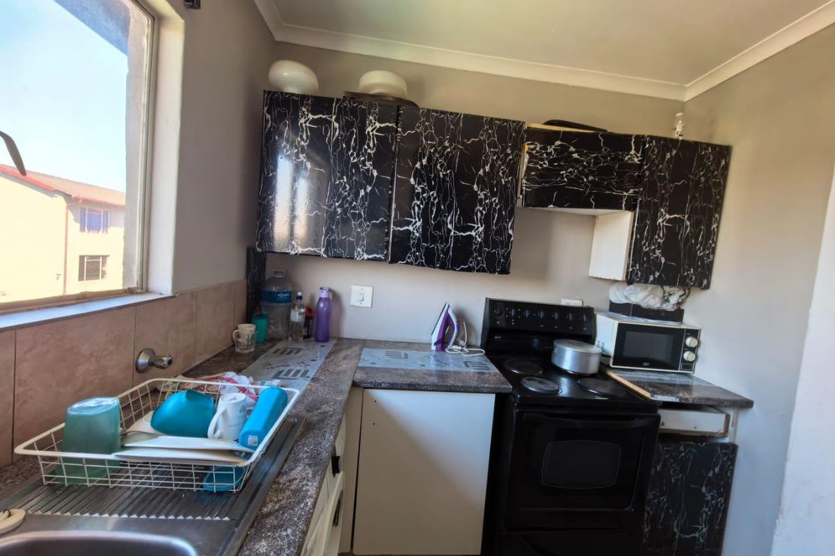 A compact kitchen featuring dark marble-effect cabinetry, laminate countertops, a stainless steel sink, and a freestanding stove with a tiled backsplash.
