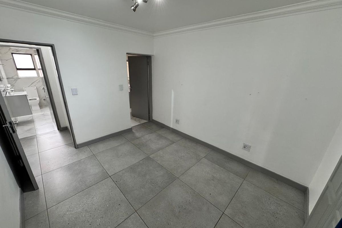 A clean, empty bedroom featuring large format grey floor tiles, crown molding, and direct access to an en-suite bathroom.