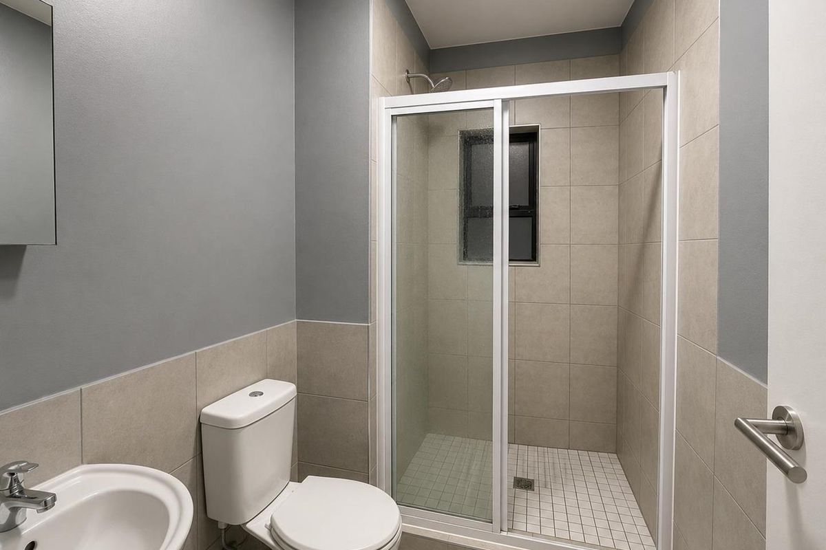 A modern bathroom featuring a glass-enclosed shower, a white ceramic toilet, and a pedestal basin with neutral wall tiling.