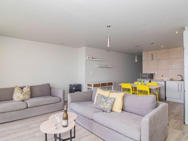Open-plan living area featuring laminate flooring, recessed lighting, and a compact kitchen with built-in cabinetry and integrated appliances.
