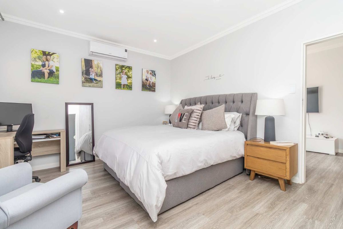 A well-maintained bedroom featuring light wood-look flooring, crown molding, and a wall-mounted air conditioning unit.