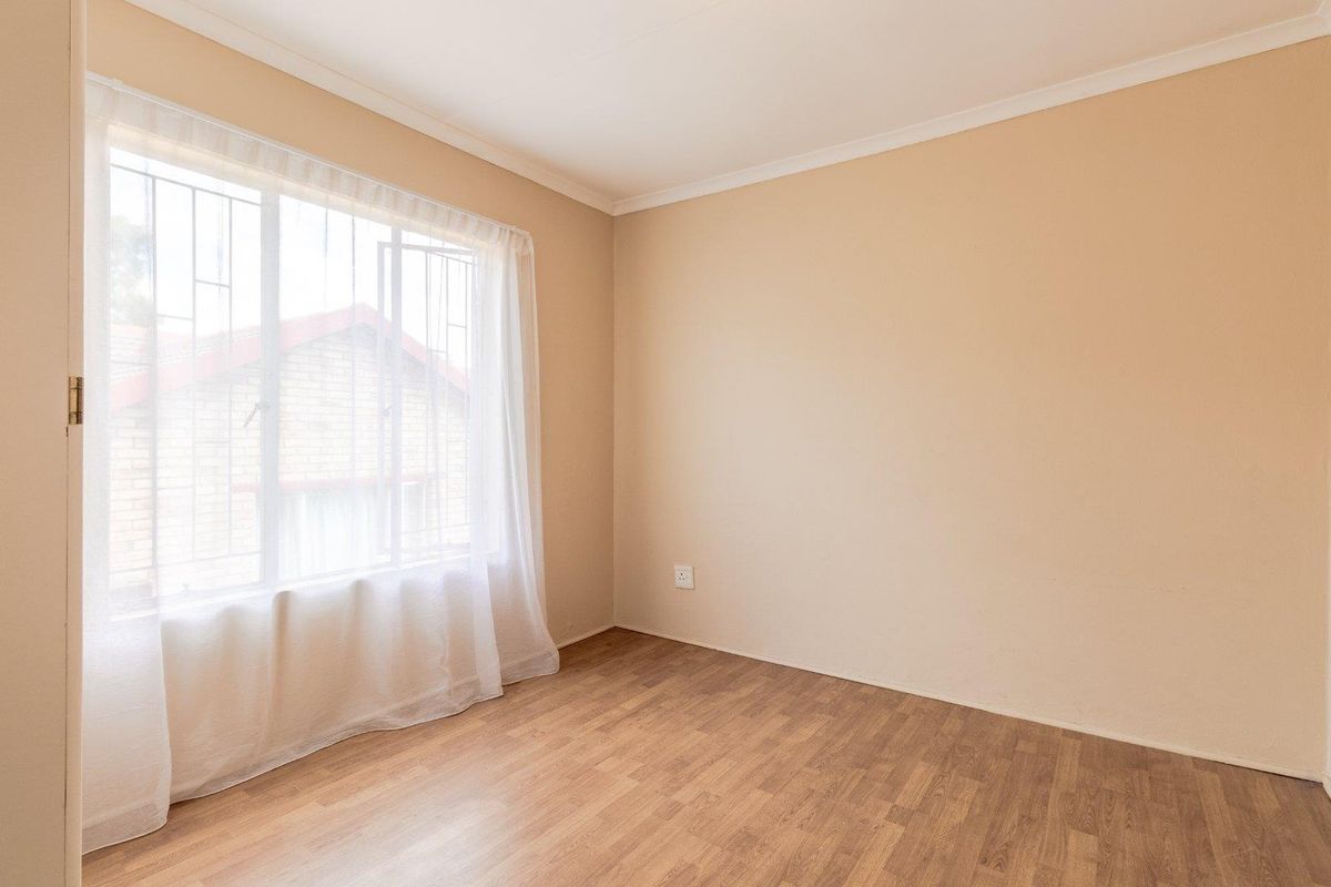 A bright, empty bedroom featuring laminate flooring, neutral walls, and a large window fitted with security bars.
